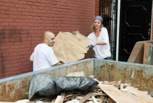 Photo of a couple filling a dumpster rental during a home renovation project.